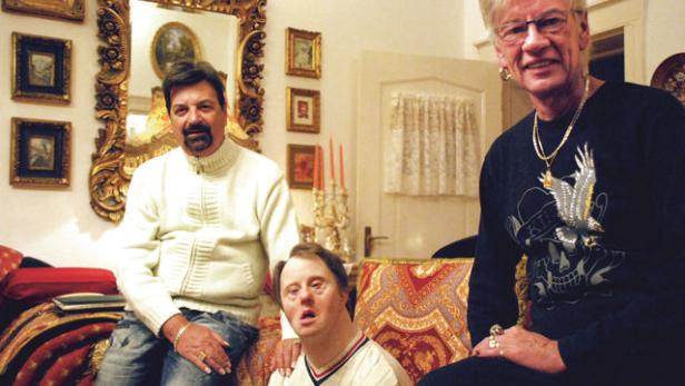 Drei Personen sitzen in einem reich verzierten Wohnzimmer.