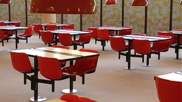 Ein Speisesaal mit roten Stühlen und Tischen unter großen, roten Lampen.