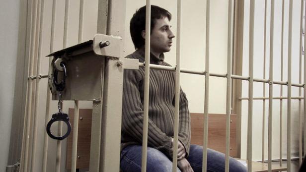 Ein Mann sitzt in einer Gefängniszelle hinter Gittern.