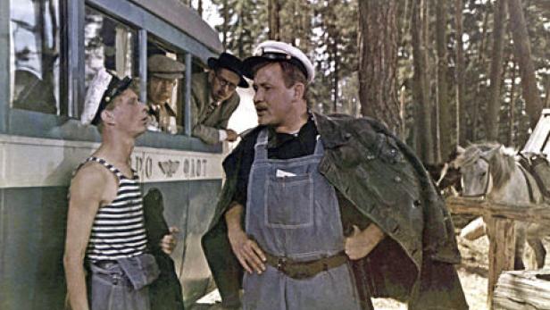 Zwei Männer in Arbeitskleidung stehen vor einem Bus in einem Waldstück.