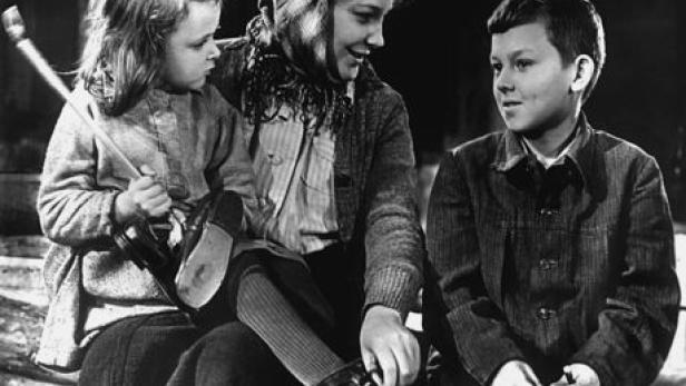 Eine Frau sitzt mit zwei Kindern, während sie einem von ihnen die Schuhe bindet.