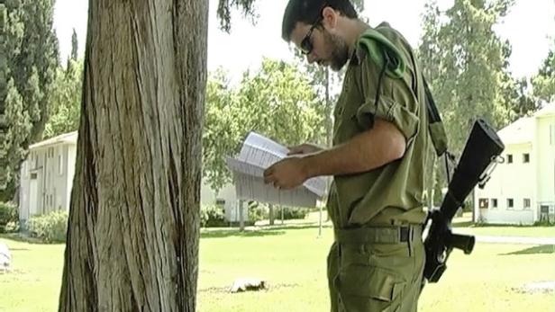 Ein Soldat in Uniform liest ein Dokument im Freien, mit einem Gewehr über der Schulter.