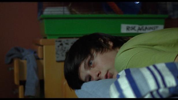 Ein junger Mann liegt auf einem blau-weiß gestreiften Kissen.