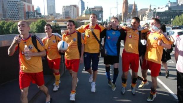 Eine Gruppe von Fußballspielern in gelb-roten Trikots geht über eine Brücke in einer Stadt.