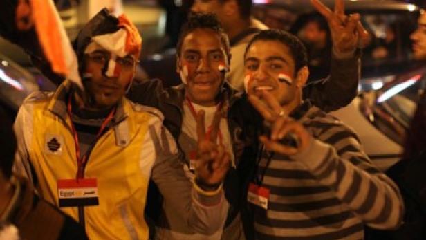 Drei junge Männer mit ägyptischen Flaggen auf ihren Gesichtern zeigen Victory-Zeichen.