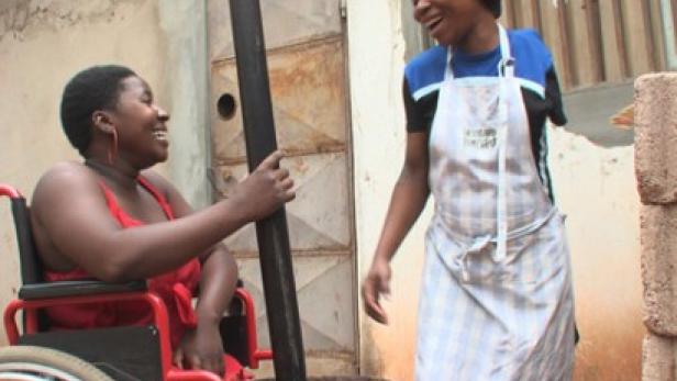 Eine Frau im Rollstuhl und eine Frau mit Schürze lachen zusammen, während sie traditionell kochen.