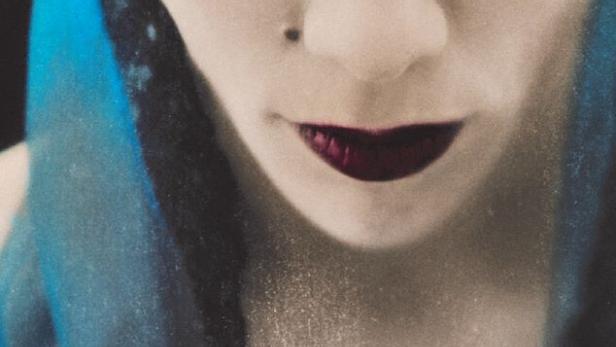 Nahaufnahme einer Frau mit dunklem Lippenstift und blauem Schleier.