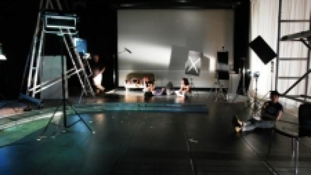 In einem Filmstudio sitzen zwei Personen vor einer Leinwand, umgeben von Filmtechnik.