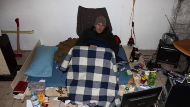 Ein Mann liegt in einem unordentlichen Raum auf einer Matratze.