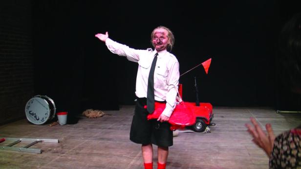 Ein Darsteller mit rußverschmiertem Gesicht auf einer Bühne mit einem roten Spielzeugauto.