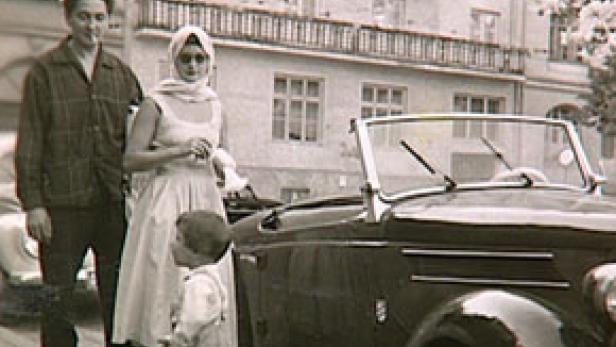 Eine Familie steht neben einem Oldtimer-Cabriolet auf einer Straße.