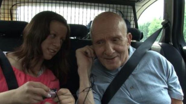 Eine junge Frau und ein älterer Mann sitzen angeschnallt im Auto.