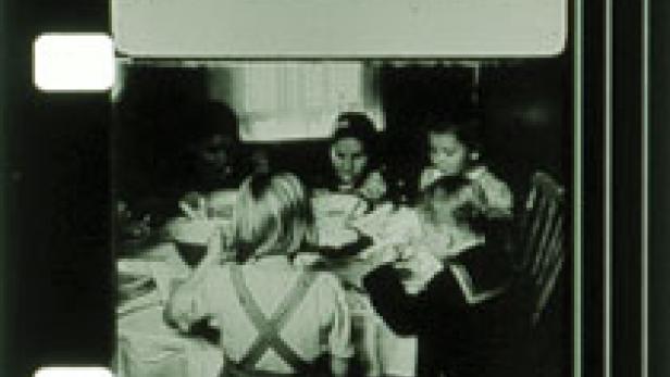 Ein Filmstreifen zeigt eine Gruppe von Kindern, die an einem Tisch essen, überlagert mit der Frage „Was gab es einen Krieg?“.