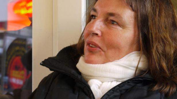 Eine Frau mit braunen Haaren und weißem Schal blickt nach oben.