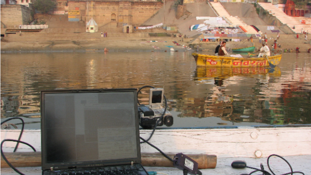 Ein Laptop und Messgeräte auf einem Boot vor der Kulisse von Varanasi am Ganges.