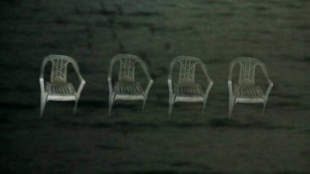 Vier leere Plastikstühle stehen im Dunkeln nebeneinander.