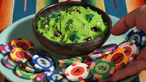 Ein Teller mit Spielchips und eine Schüssel mit grünem Teig, dekoriert mit Würfeln und Spielhäusern.