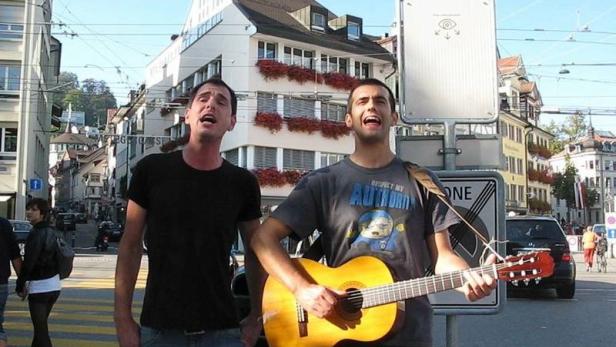 Zwei Männer stehen auf einer Straße und singen, einer spielt Gitarre.