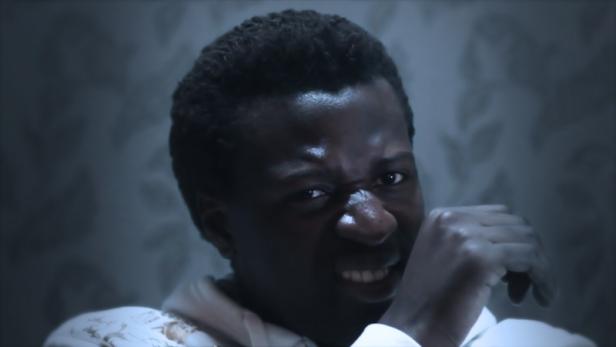 Ein Mann blickt grimmig in die Kamera, die Faust vor dem Mund.