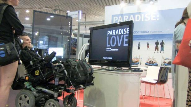 Ein Mann im Rollstuhl schaut sich den Filmtitel „Paradise Love“ auf einem Bildschirm an.