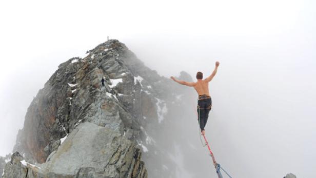 Ein Mann balanciert auf einer Slackline zwischen zwei Berggipfeln.
