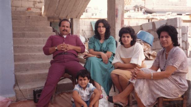 Eine Familie sitzt im Freien vor einem unfertigen Gebäude.