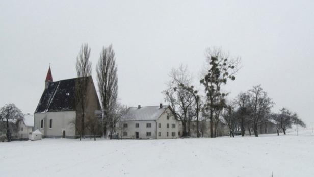 Eine verschneite Landschaft mit einer Kirche und einigen Häusern.