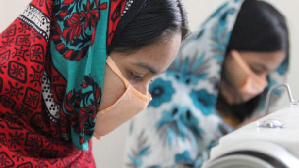Zwei Frauen mit Gesichtsmasken arbeiten an Nähmaschinen.