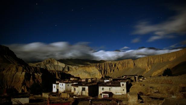 Ein Dorf liegt nachts in einem Tal unter einem sternenklaren Himmel.