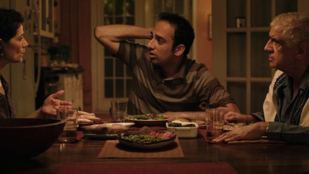 Drei Personen sitzen an einem Tisch mit Speisen und scheinen sich angeregt zu unterhalten.