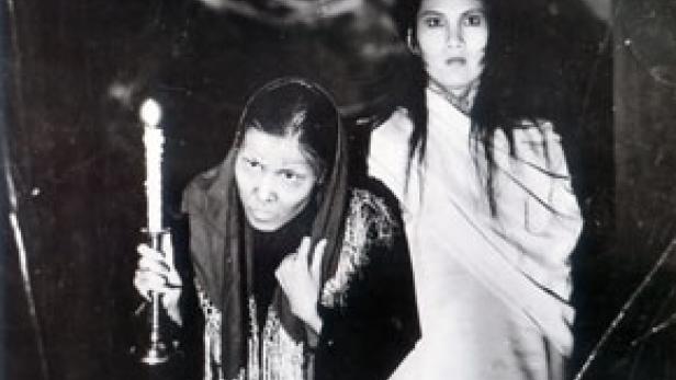 Zwei Frauen, eine mit einer Kerze, posieren in einem Schwarzweißfoto.