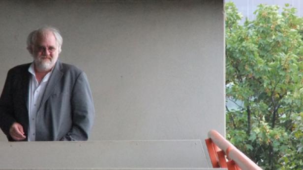 Ein Mann mit Bart und Brille steht auf einer Treppe vor einem Gebäude.