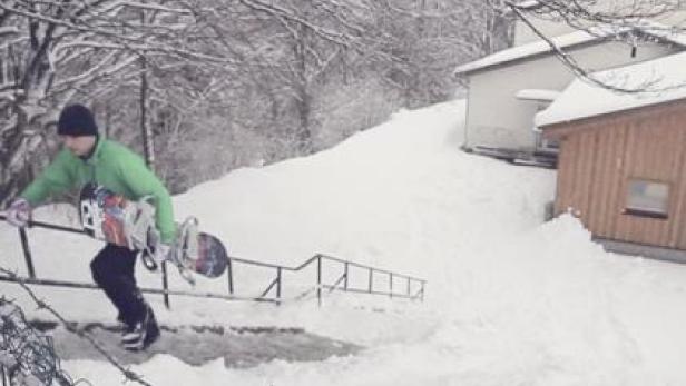 Ein Mann mit Snowboard steigt eine verschneite Treppe hinauf.