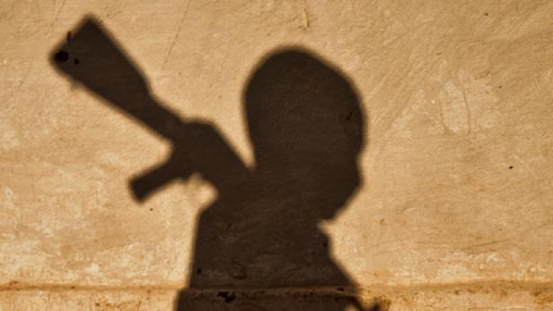 Der Schatten eines Kindes, das mit einem Spielzeuggewehr spielt, ist an einer Wand zu sehen.