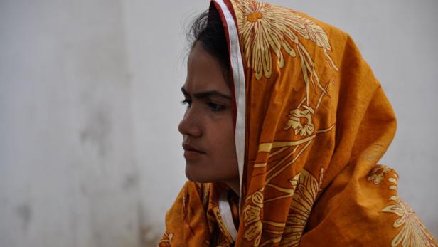 Eine junge Frau mit einem orangefarbenen Kopftuch mit Blumenmuster.