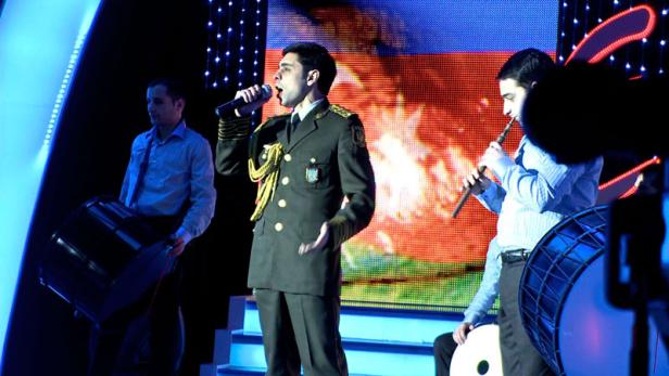 Ein Sänger in Uniform tritt mit Musikern auf einer Bühne auf.