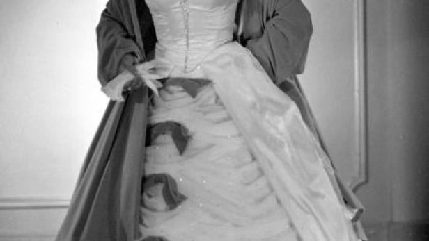 Eine Frau in einem eleganten Ballkleid mit Schleifen und einem Tuch über den Schultern.