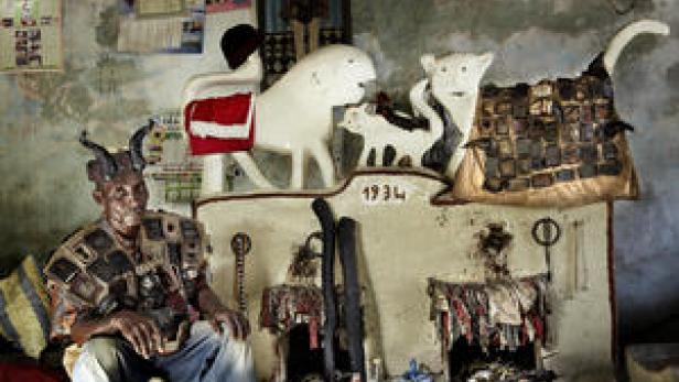 Ein Mann in traditioneller Kleidung sitzt vor einem Altar mit Voodoo-Symbolen.