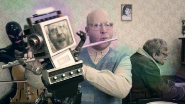 Ein Mann spielt Flöte, während ein Roboter, eine maskierte Person und eine weitere Person musizieren.