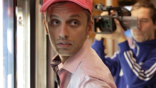 Ein Mann mit rosa Kappe wird von einem Kameramann gefilmt.