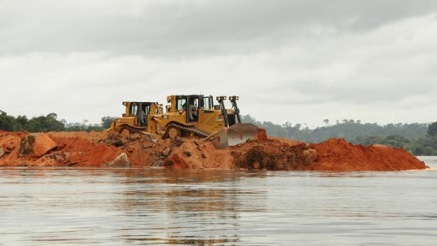 Zwei gelbe Bulldozer schieben Erde in einem Gewässer zusammen.