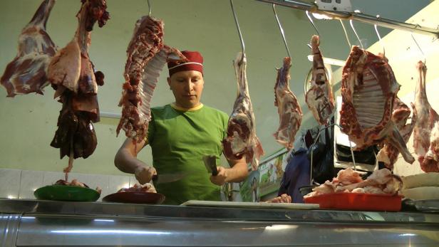 Ein Metzger mit roter Mütze zerteilt Fleisch in einem Schlachtbetrieb.