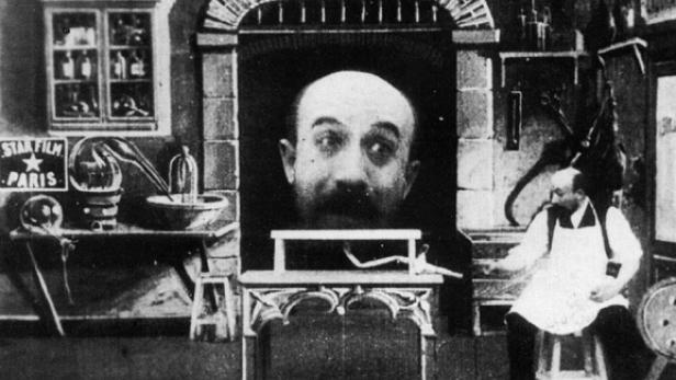 Ein Mann sitzt vor einer riesigen schwebenden Kopfattrappe in einem Filmstudio.