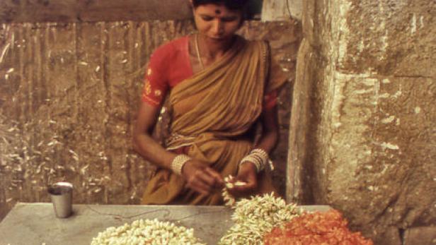 Eine Frau in einem Sari fertigt Blumengirlanden an einem Stand.