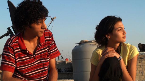 Ein junger Mann und eine junge Frau sitzen auf einem Dach und schauen in die Ferne.