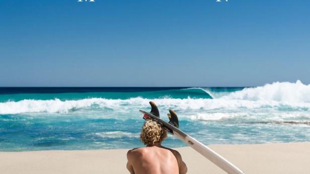 Ein Mann sitzt mit einem Surfbrett am Strand und blickt auf das Meer. Das Filmplakat wirbt für „View From a Blue Moon“.