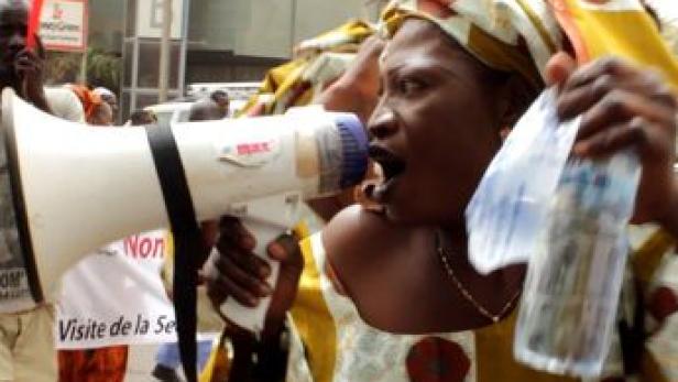 Eine Frau ruft mit einem Megaphon auf einer Demonstration, während sie eine Wasserflasche hält.