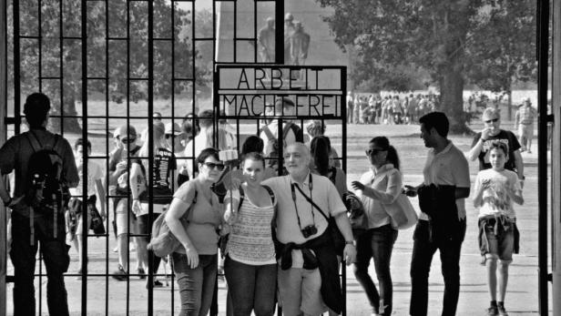 Besucher stehen vor dem Tor mit der Aufschrift „Arbeit macht frei“ in einem Konzentrationslager.
