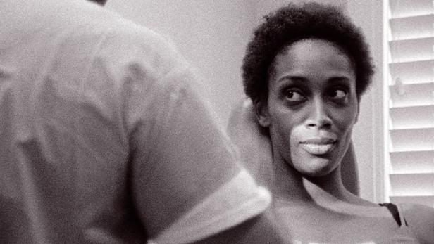 Eine Frau mit kurzen, lockigen Haaren schaut über ihre Schulter.