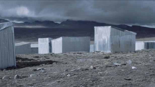 Mehrere kleine Gebäude aus Wellblech in einer kargen Landschaft unter einem dunklen Himmel.